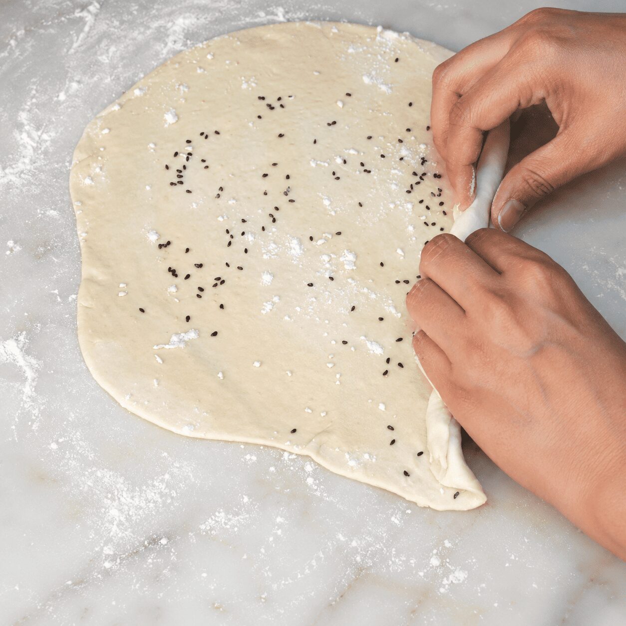 Rolling dough thin and spreading ghee, maida, and kalonji for layered paratha